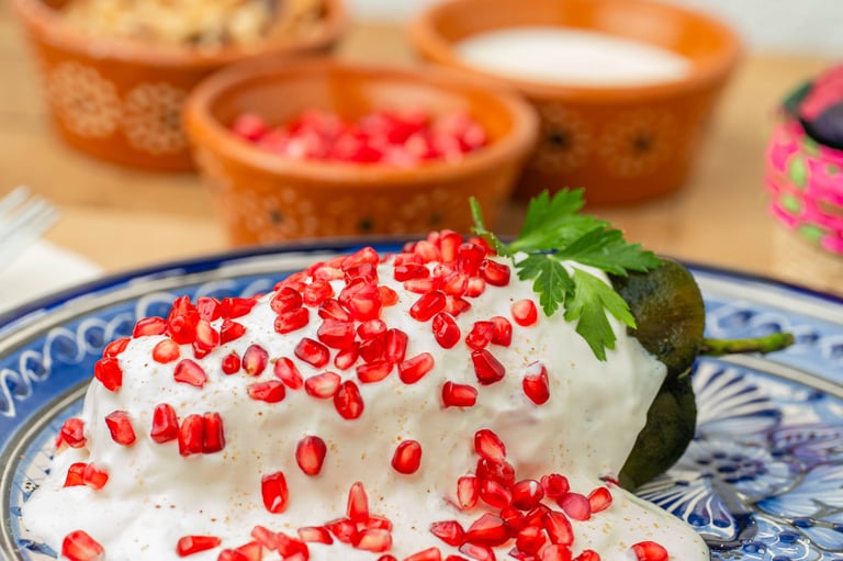 Chilaquiles in nogada topped with red pomegranate seeds and mint leaf on decorative blue and white plate