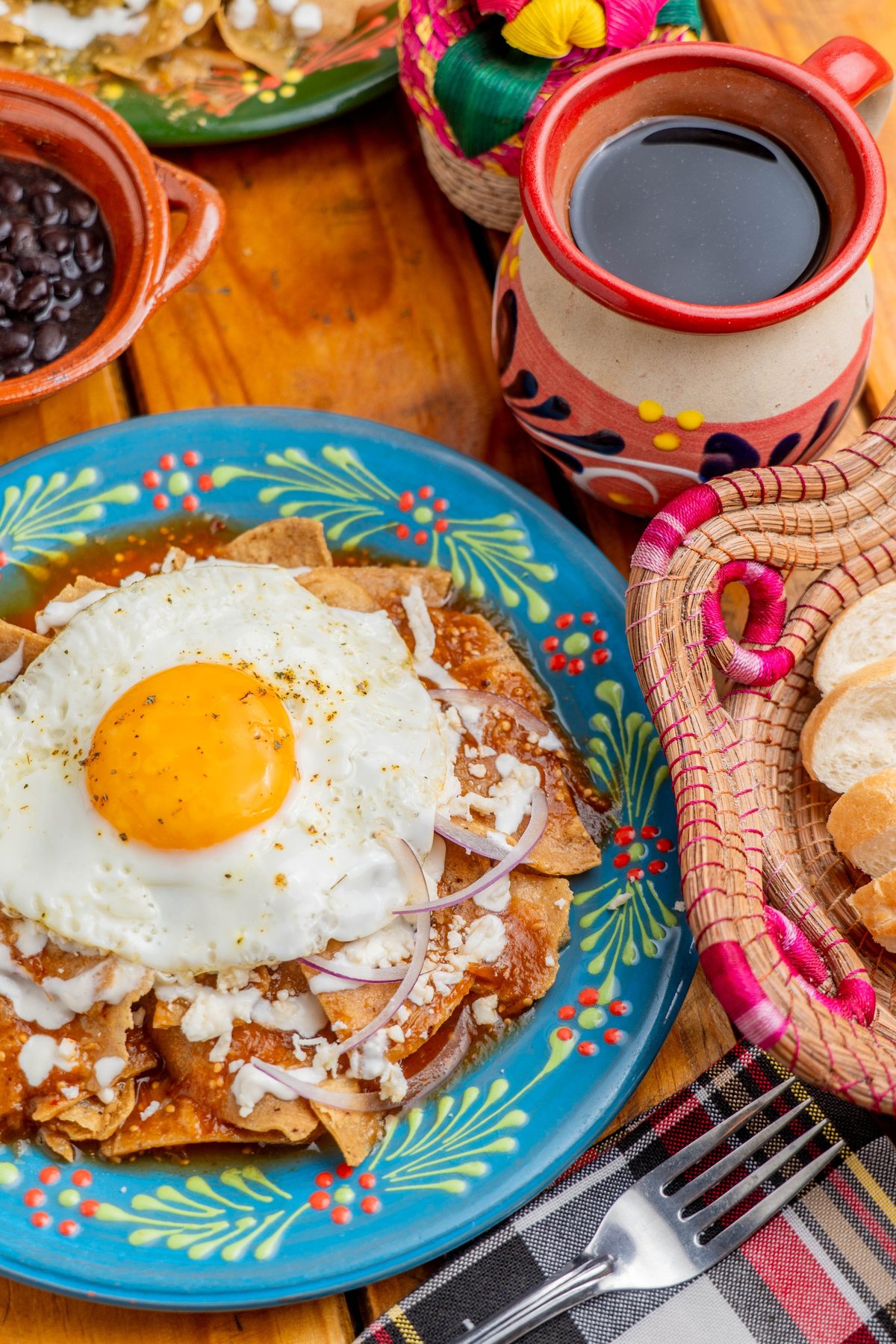Fried egg on crispy tortilla with cheese and onions on colorful plate, served with traditional Mexican breakfast items