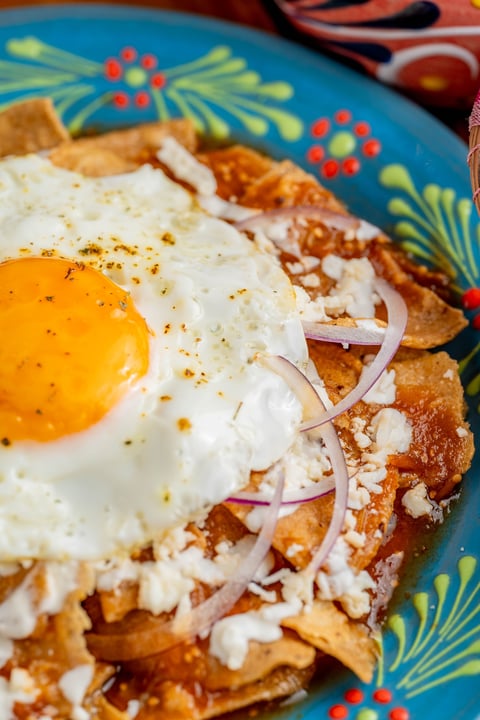Fried egg and sliced onions on crispy fried chilaquiles served on a colorful blue plate with decorative patterns.